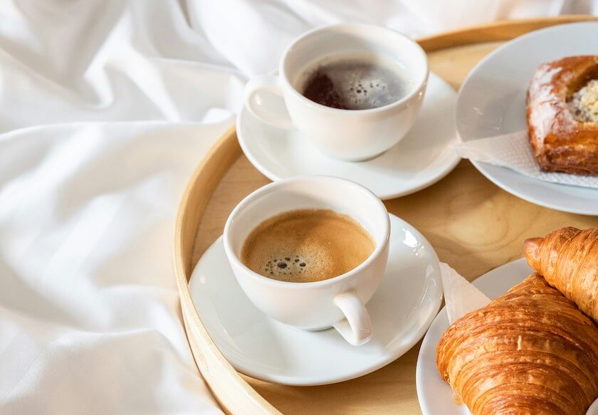 A breakfast tray of coffee and croissants sits on a bed representing a weekly tradition.