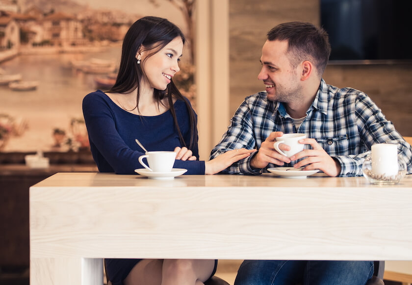 Couple sit having coffee in a cafe, talking with ease and understanding sharing a calm and connected moment together.
