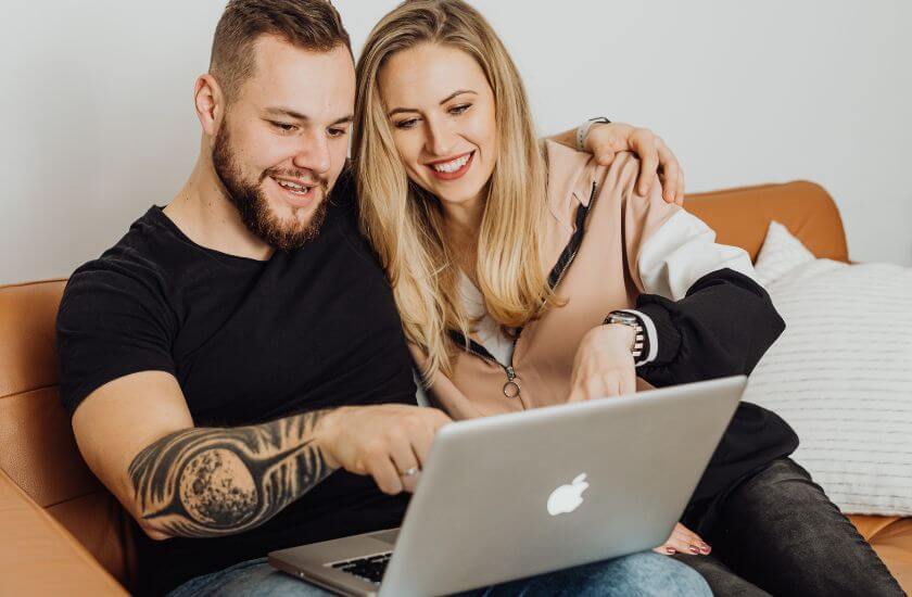 Couple sit on a sofa pointing at the ritual guide on a laptop to help them strengthen daily connection.