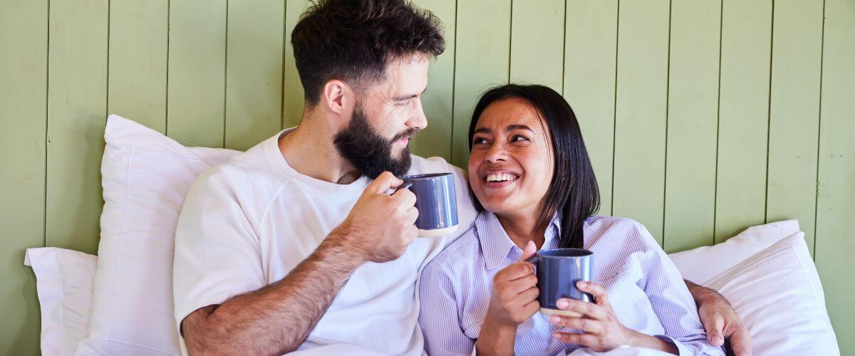Couple sit up in bed having a morning coffee checking in with each other.