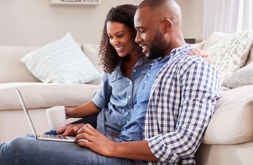 Couple sit on the floor against a sofa exploring the marriage journal on a laptop.