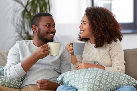 Couple sit on sofa talking having coffee forming the foundations of their relationship.