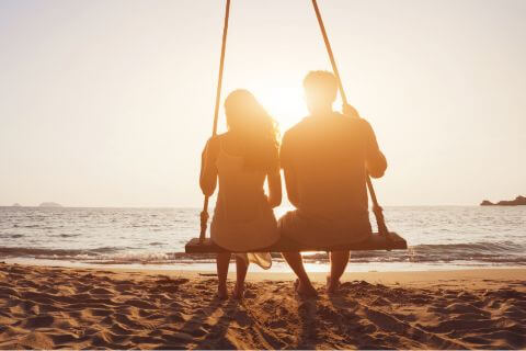 Newlywed couple sit on a swing on the beach reflecting on closeness and affection evolve.
