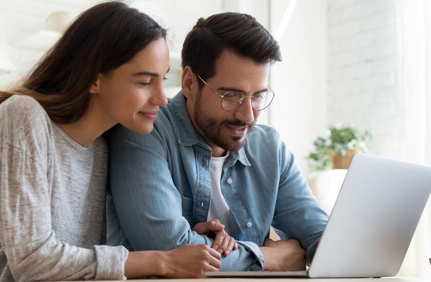 Newlywed couple sit close together looking at the communication guide on a laptop.