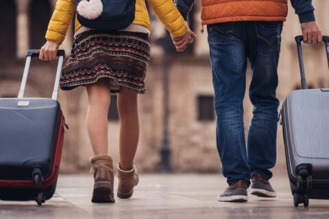 Couple walk holding hands as the pull suitcases representing historical baggage they bring to marriage.