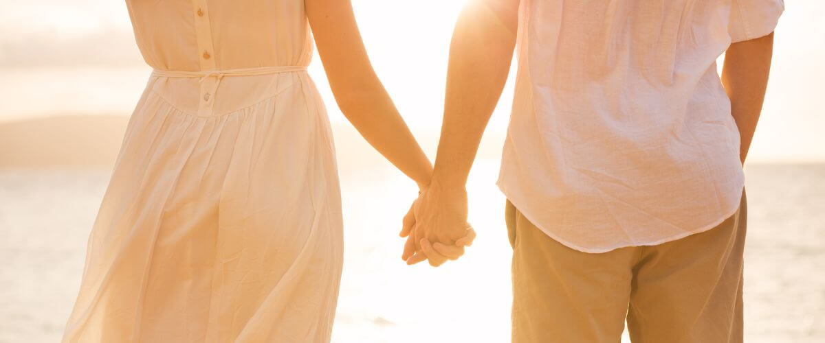 Couple hold hands on beach looking out to sea reflecting on what influences their relationship.