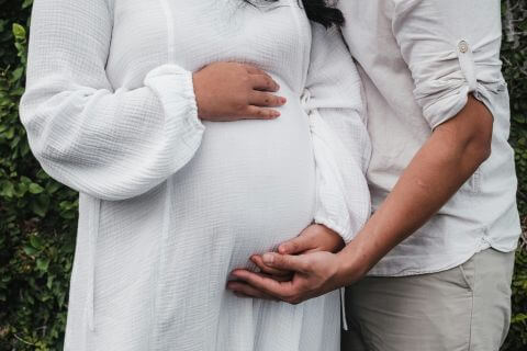 Husband cuddles his expectant wife, both touching her tummy representing a typical marriage.