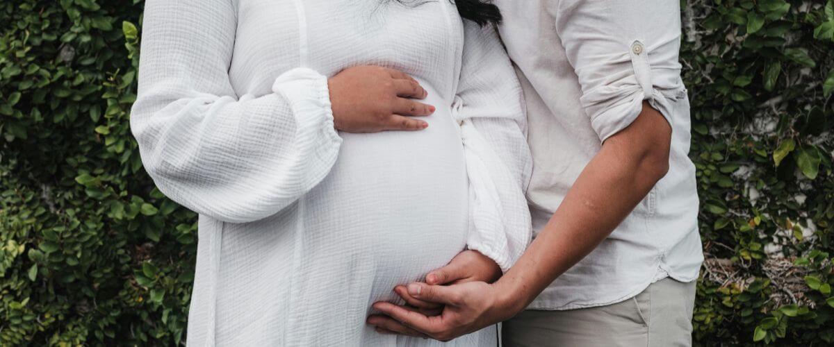 Husband cuddles his expectant wife, both touching her tummy representing a typical marriage.