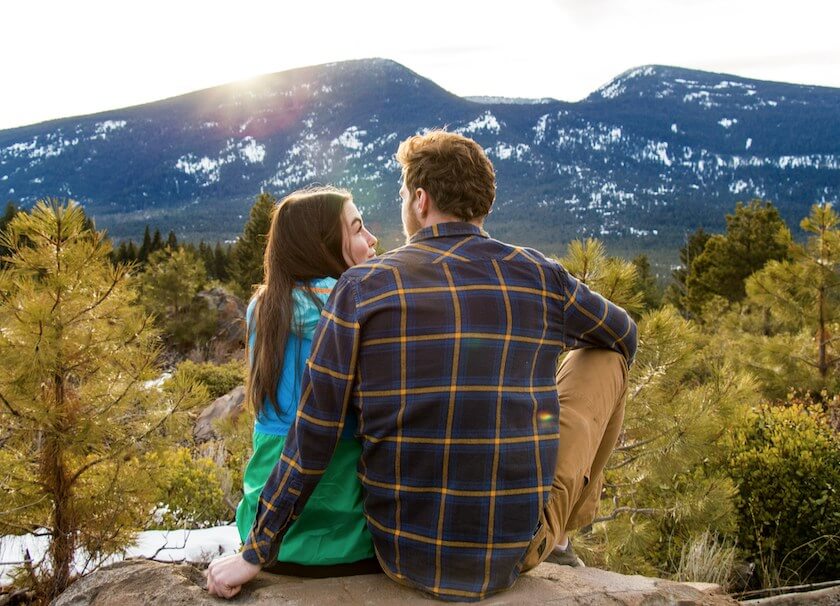 Couple sit on rock with snow capped mountains in the horizon reflecting on.