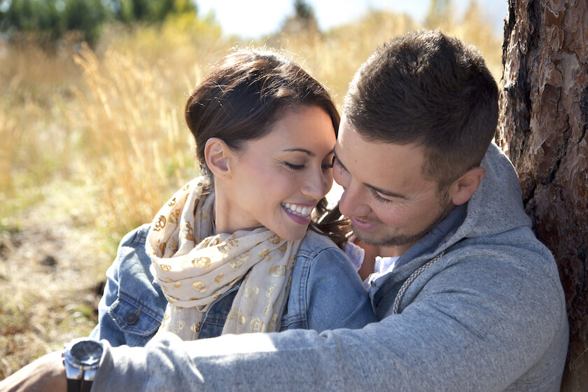 Couple cuddle by a tree as they rest on their walk, reflecting on their intimacy