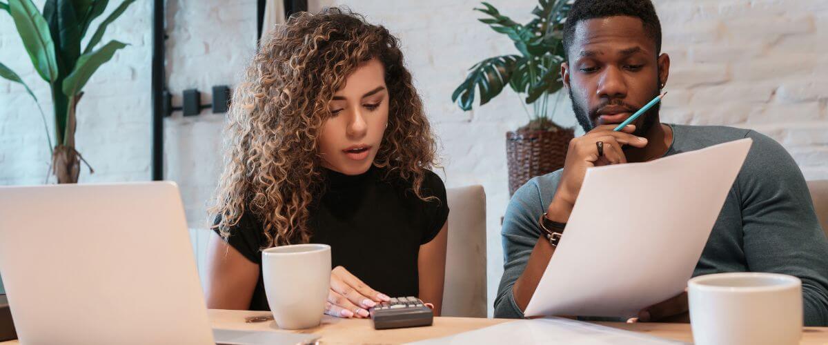 Couple sit at a table with laptop and paperwork, managing financial stress in early marriage